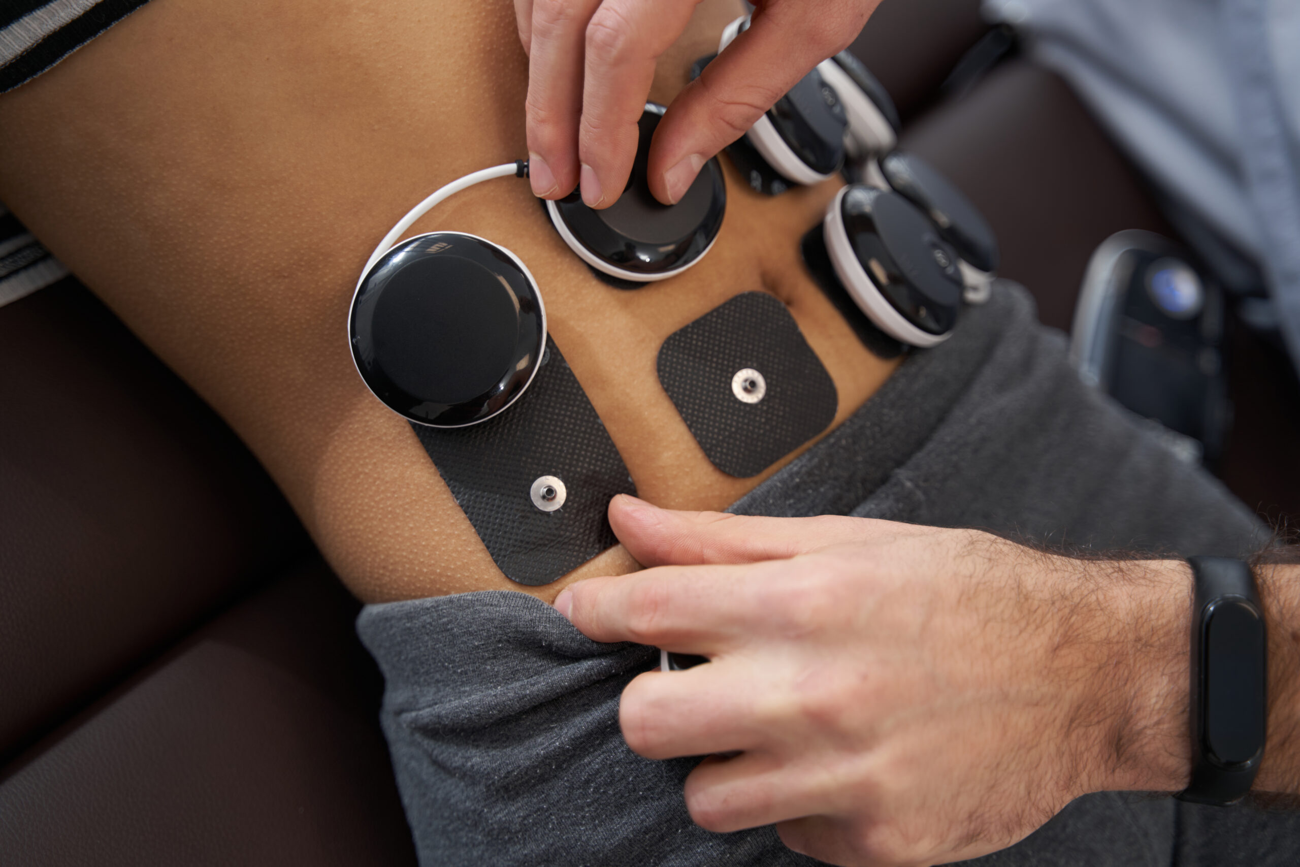 Close-up photo of lady lying on couch, medical worker standing near and attaches electrical muscle stimulator to her abdomen